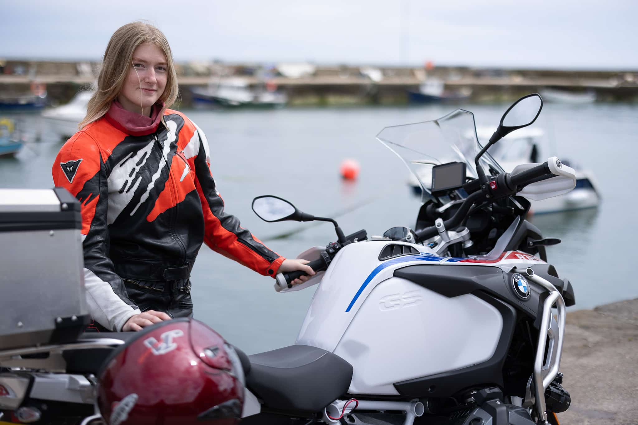A beautiful, blonde-haired girl standing behind a big motorbike, dressed in colourful leathers, photographed by Julian Davies Photography in Aberdeenshire