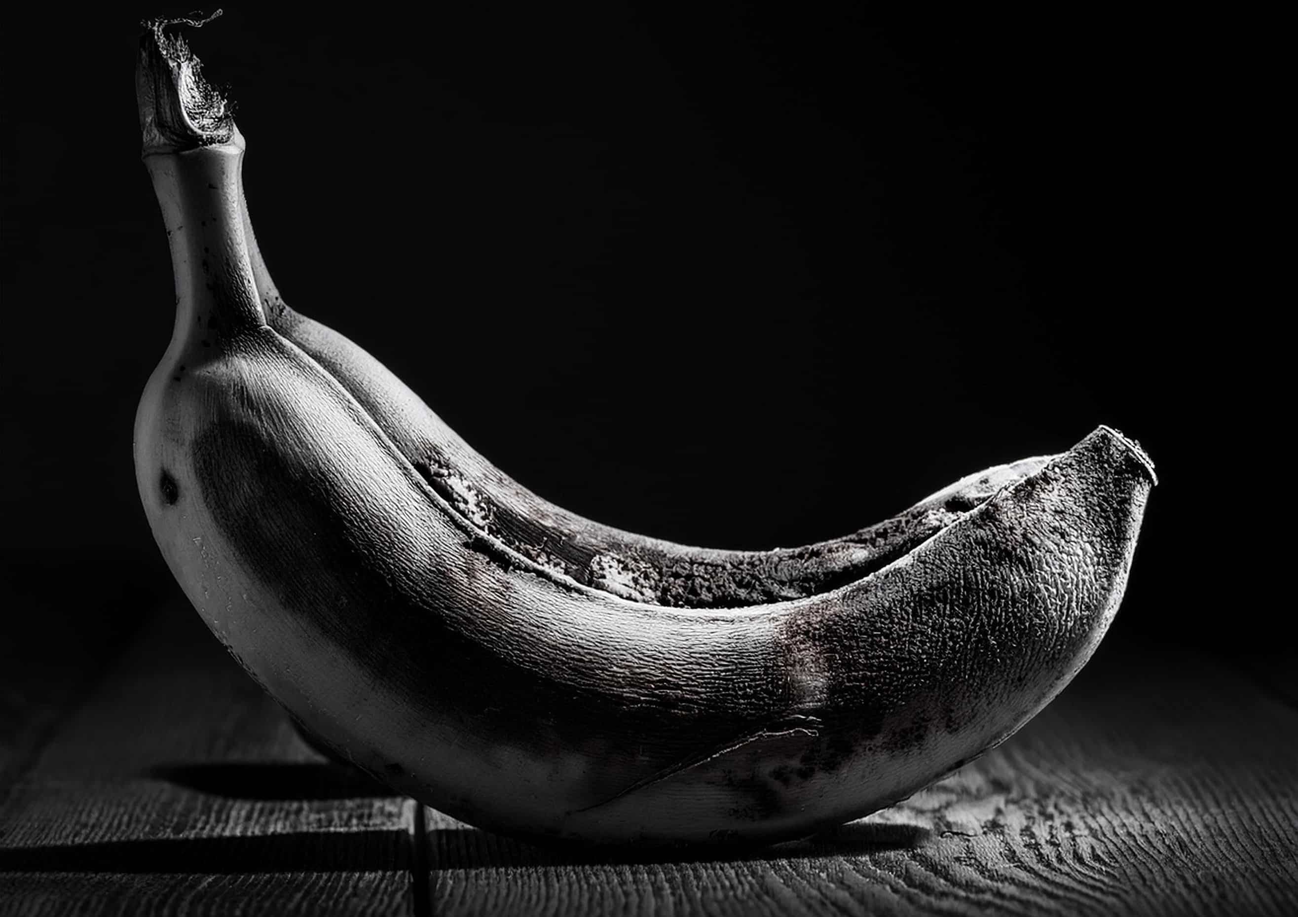 A detailed black and white photograph of a rotting banana, showcasing its textured skin and soft interior, captured in the Julian Davies Photography studio based in Aberdeenshire.